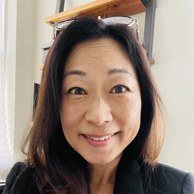 Christina Lee Kim, PhD, smiling, with reading glasses pushed up on her head
